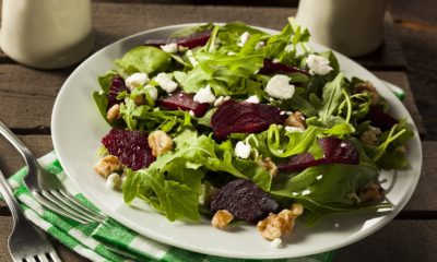 White plate with roasted beet slices, chopped walnuts and feta cheese on a bed of greens