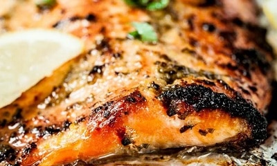 Close up of baked salmon on foil with wedges of lemon and fresh green herbs